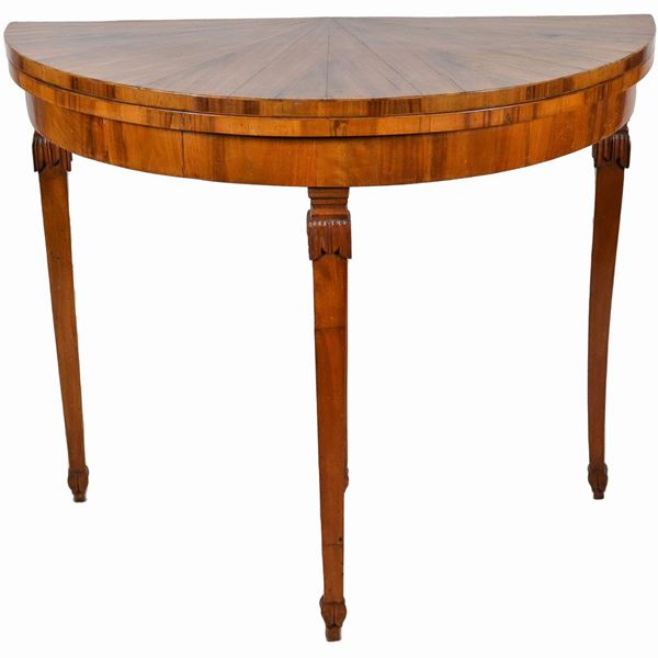 Tavolo da gioco a demi- lune in noce, con piano ribaltabile, quattro gambe a tronco di piramide rovesciata con intagli, di cui una estraibile