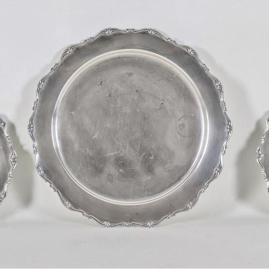 Lotto di tre piatti tondi in argento con bordi cesellati e sbalzati a volute e palmette, uno grande e due piccoli, gr. 1040