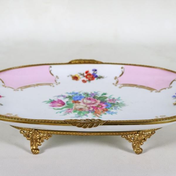 Oval centerpiece in polychrome Limoges porcelain with relief decorations with motifs of bunches of flowers, handles, border and four feet in gilded, embossed and chiseled metal