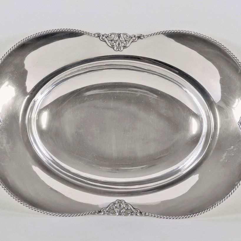 Centrotavola a forma sagomata in argento con bordo cesellato e sbalzato a volute e trafori, sorre...