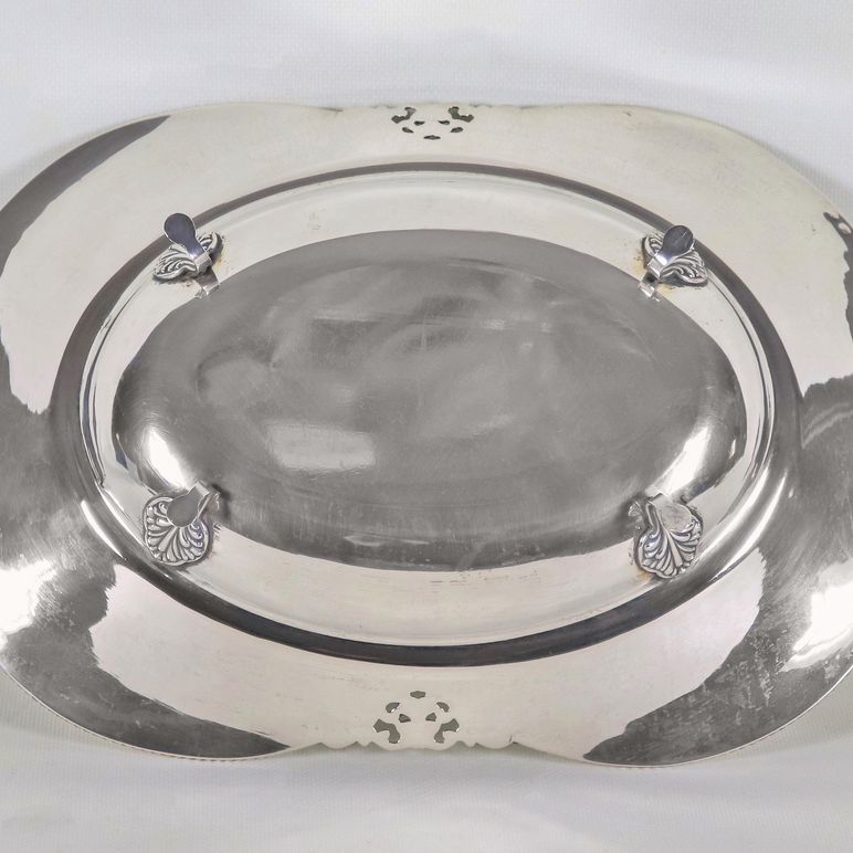 Centrotavola a forma sagomata in argento con bordo cesellato e sbalzato a volute e trafori, sorre...