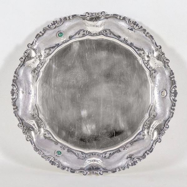 Piatto tondo in argento con bordo cesellato e sbalzato a volute, conchiglie e applicazioni di pietre dure verdi, una mancante, gr. 570