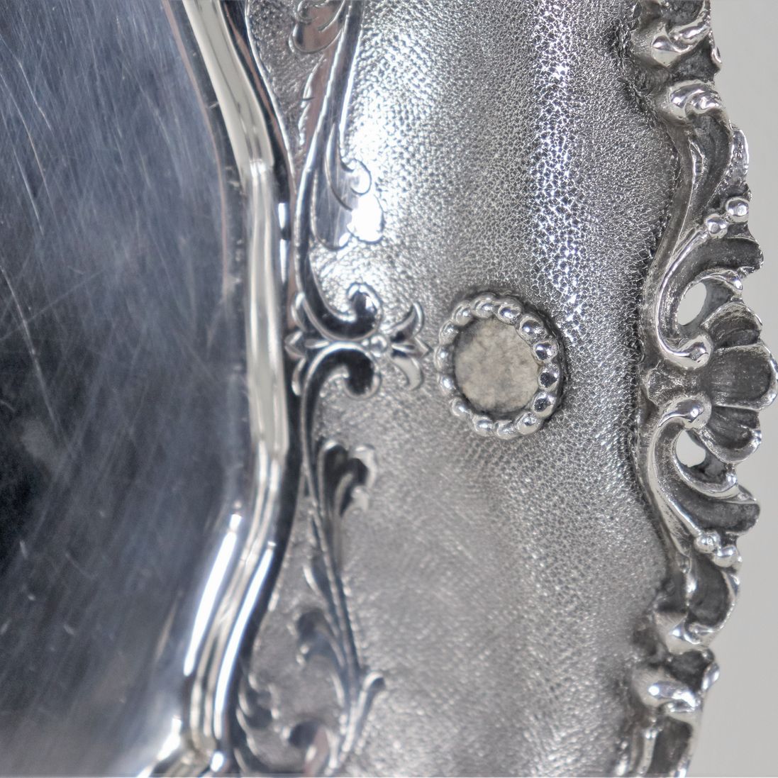 Piatto tondo in argento con bordo cesellato e sbalzato a volute, conchiglie e applicazioni di pie...