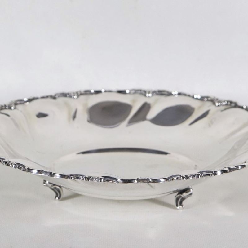 Piccolo centrotavola tondo in argento con bordo cesellato e sbalzato a volute, sorretto da tre pi...