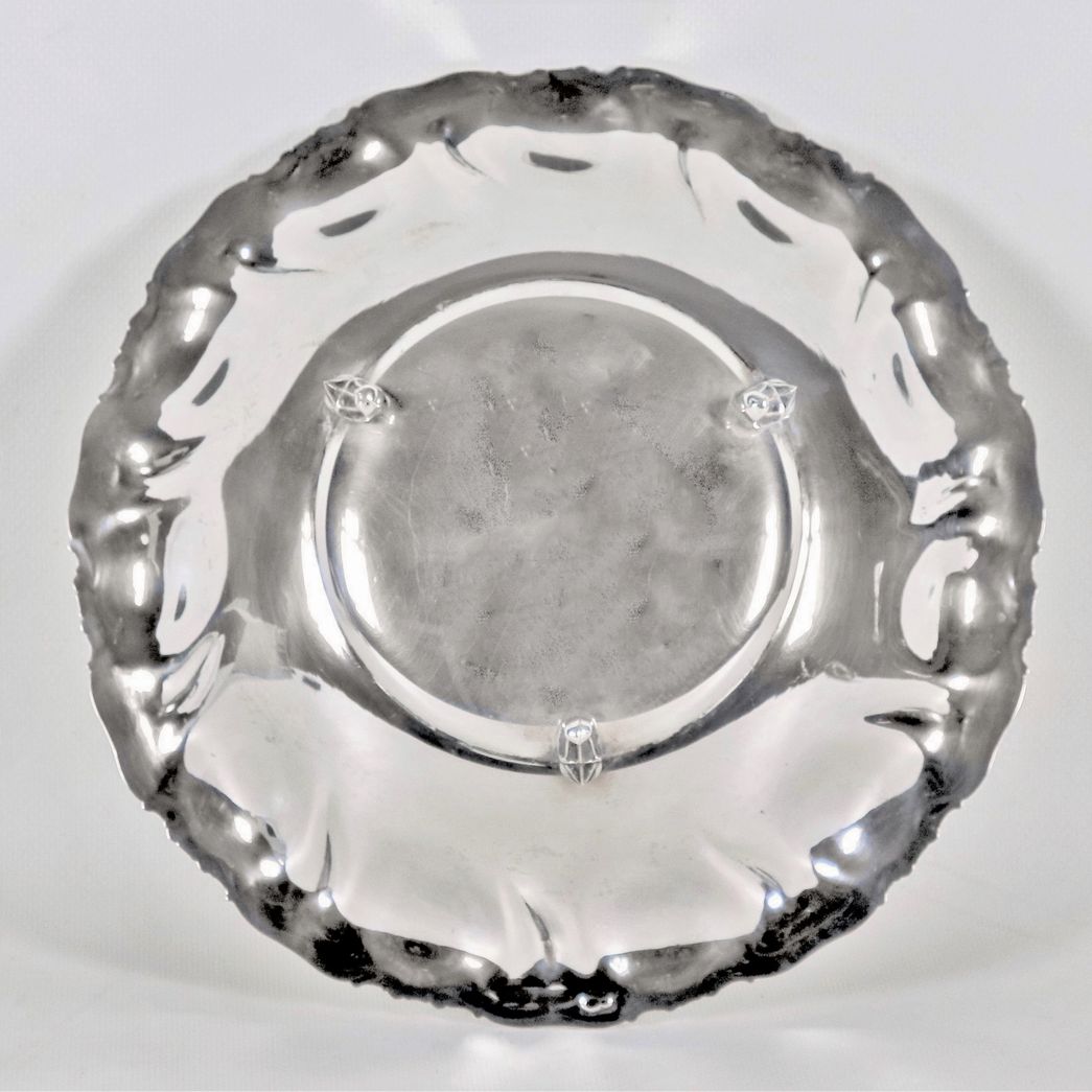 Piccolo centrotavola tondo in argento con bordo cesellato e sbalzato a volute, sorretto da tre pi...