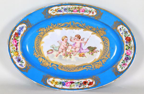 Antico piatto ovale da muro in porcellana francese di Sèvres, interamente decorato e variopinto con allegorie di putti e intrecci floreali su fondo celeste e oro zecchino