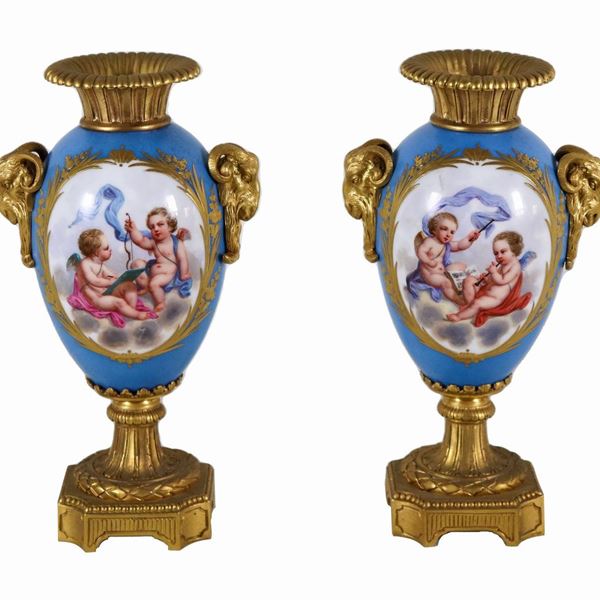 Pair of ancient small vases in French Sèvres porcelain and gilded bronze, with colorful medallions with motifs of allegories of cherubs and bunches of flowers on a blue background, handles in the shape of goats' heads with laurel wreaths