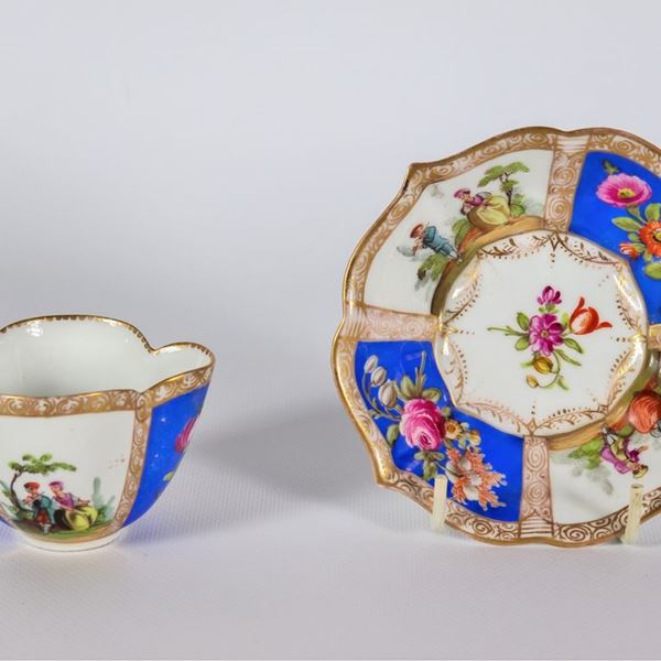 Tazza con piattino in porcellana tedesca bianca e blu, con decorazioni policrome di scene galanti e mazzetti di fiori, piccola mancanza al manico della tazza