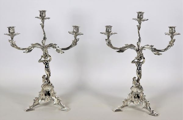 Coppia di candelabri in argento cesellato e sbalzato, con piccole sculture di putti, 3 fiamme ciascuno, gr. 2300