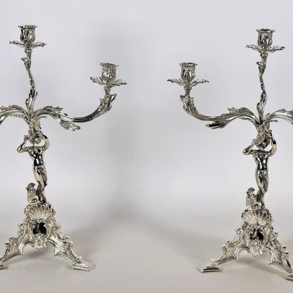 Coppia di candelabri in argento cesellato e sbalzato, con piccole sculture di putti, 3 fiamme ciascuno, gr. 2300