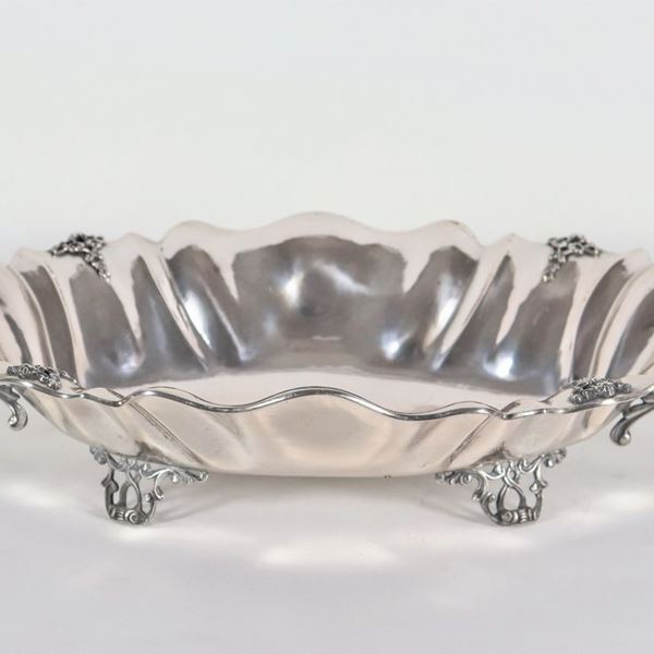 Grande centrotavola in argento sbalzato e cesellato, a forma ovale centinata con manici a foglie d'acanto, sorretto da quattro piedini traforati, gr. 1115