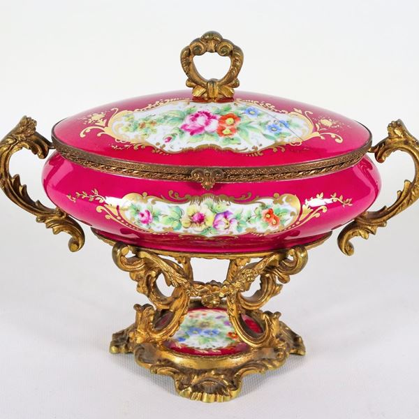 Scatola ovale francese in porcellana rossa, con decorazioni variopinte a mazzetti di fiori, manici e base in bronzo dorato, sbalzato e cesellato