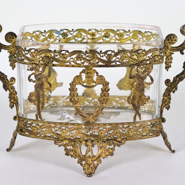 Centrotavola ovale francese in metallo dorato, cesellato e sbalzato a motivi Impero di vestali danzanti, putto e cornucopie, all'interno vaschetta in cristallo con varie rotture e danneggiamenti