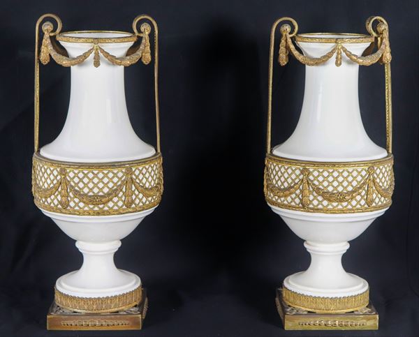 Pair of amphorae in white glazed and porcelain ceramic, with gilt and chiseled bronze trimmings, handles and bases with Louis XVI motifs