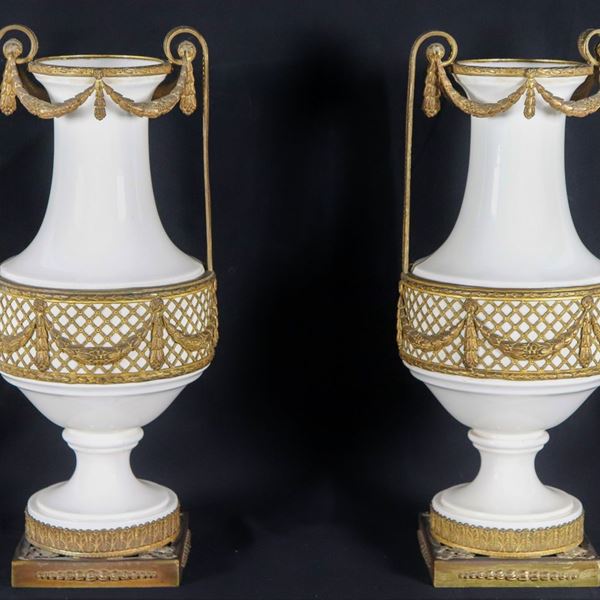 Coppia di anfore in ceramica bianca smaltata e porcellanata, con guarnizioni, manici e basi in bronzo dorato e cesellato a motivi Luigi XVI