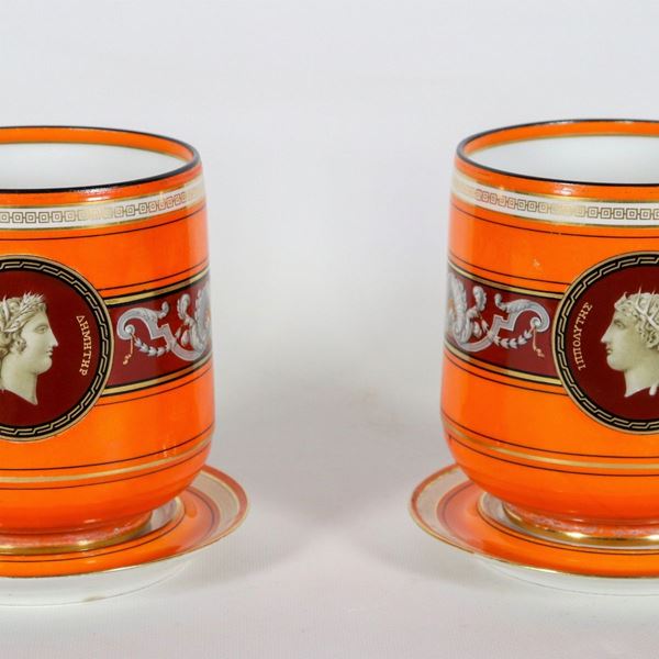 Coppia di piccoli cachepots con sottopiatti in porcellana francese di linea neoclassica, con decorazioni a volute e conchiglie e medaglioni centrali con i profili di "Demetra" e "Ippolito"