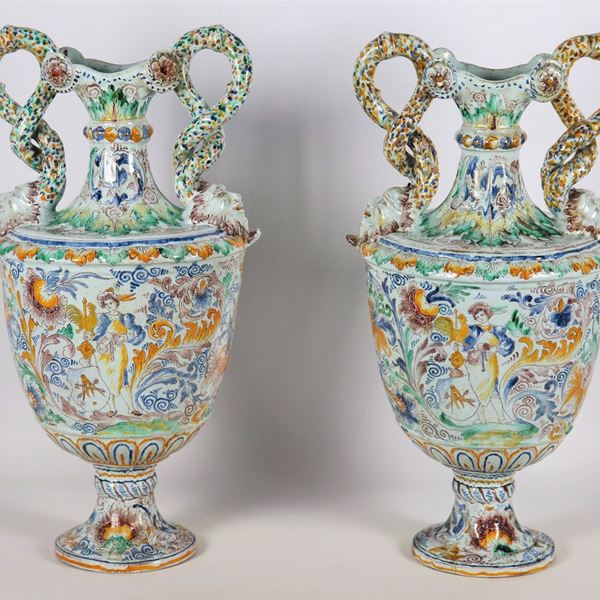 Coppia di anfore in maiolica italiana smaltata, interamente decorate con intrecci floreali e figure di dame e pastorelle, manici a forma di serpenti terminanti a mascheroni