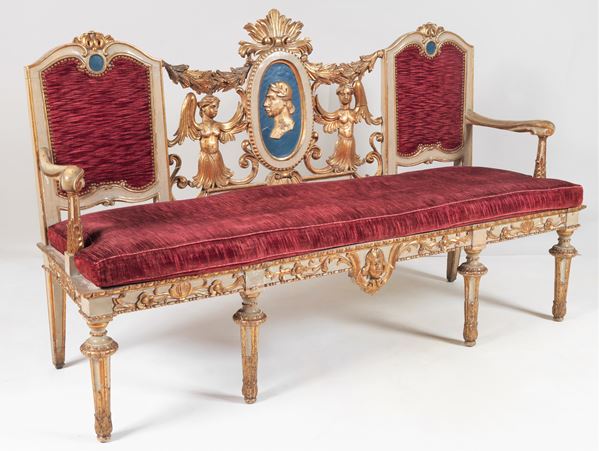 Divano Luigi XVI in legno laccato, dorato e intagliato con al centro dello schienale medaglione con profilo di "Antico Romano" e sculture di figure muliebri ai lati, copertura in velluto rosso