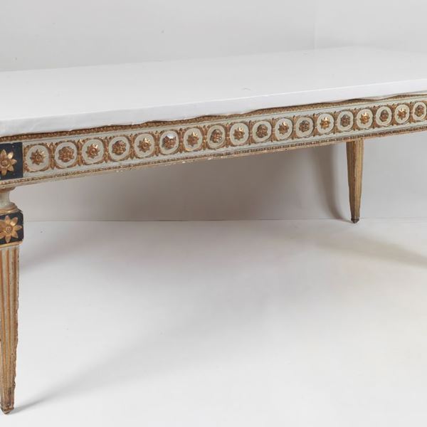 Tavolo da pranzo rettangolare di linea Luigi XVI in legno laccato avorio e dorato, con intagli a motivi neoclassici. Mancante del piano in marmo, sostituito da piano in legno rivestito