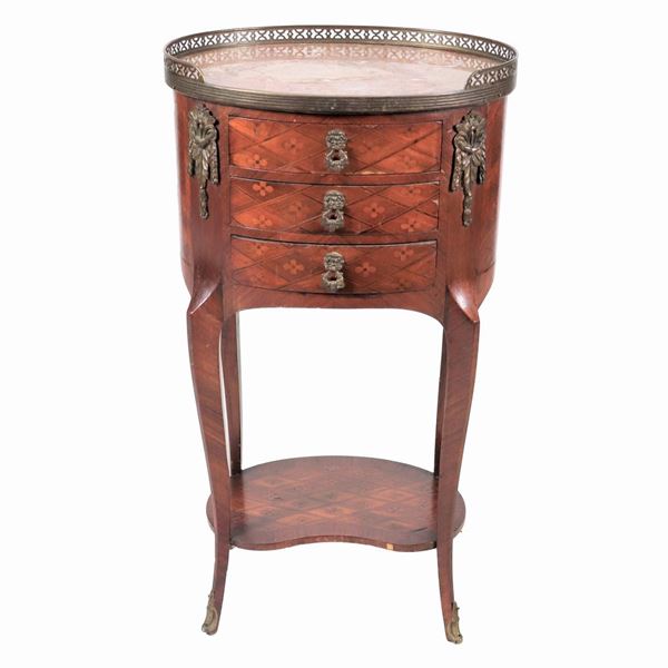 Gueridon francese ovale di linea Luigi XVI in mogano e bois de rose, con intarsi a marqueterie, piano in marmo con ringhierina, fregi e guarnizioni in bronzo dorato e cesellato, tre tiretti e quattro gambe ricurve riunite da pianetto sottostante sagomato