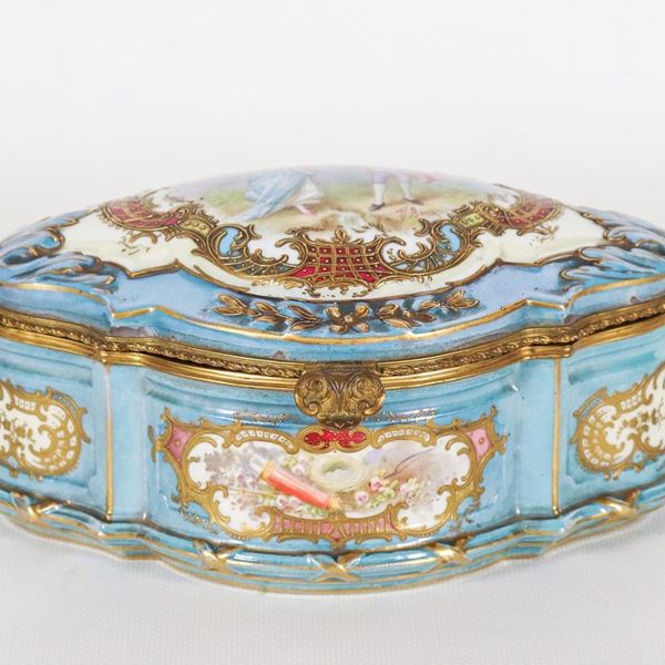 Oval box in light blue Sèvres porcelain, with relief highlights in pure gold and painted squares with intertwining floral motifs and arch with quiver, painted scene signed "The courtship" on the lid