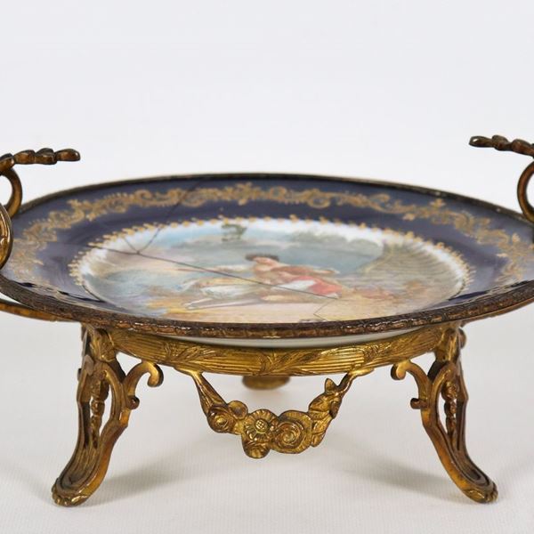 Alazata tonda in porcellana di Sèvres, con bordo in blu cobalto e oro zecchino, al centro scena dipinta firmata "Mamma con figlioletto", manici e base in bronzo dorato e cesellato. Rotture