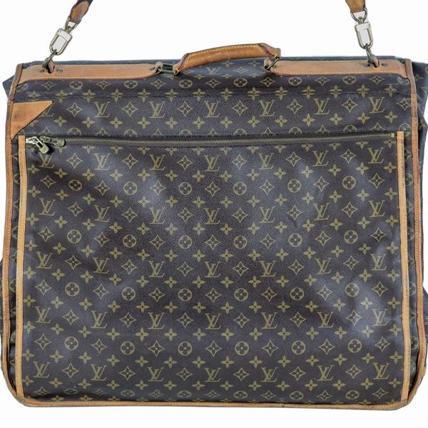 Porta abiti Louis Vuitton in tela monogram marrone con rifiniture in vacchetta naturale, grande tasca con zip sul davanti, manico in pelle e tracolla regolabile rimovibile in tela, tiralampo in ottone logati, gancio e moschettoni di chiusura in ottone e piedini per appoggio