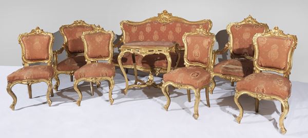 Ancient Neapolitan Louis Philippe lounge (1830-1848), in gilded wood and richly carved with shell motifs, scrolls of acanthus leaves and flowers: sofa, two armchairs, four chairs and center table (8 pieces). The edge underneath the sofa seat is broken