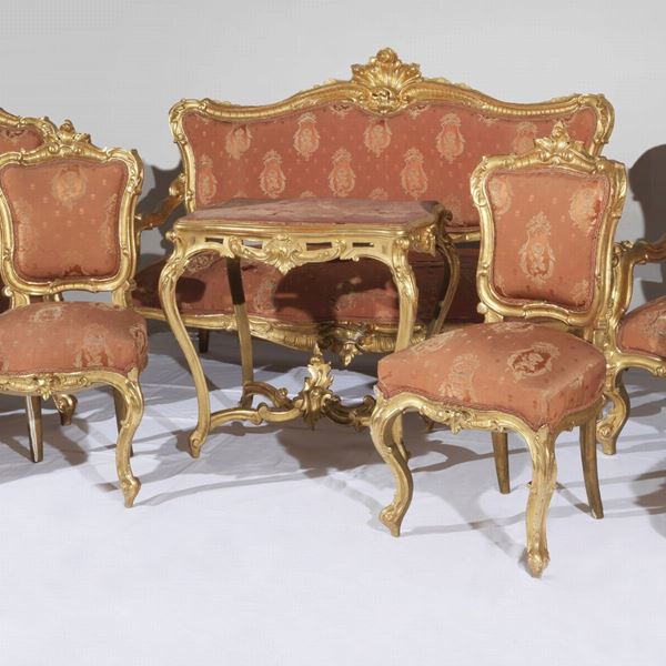 Antico salotto napoletano Luigi Filippo (1830-1848), in legno dorato e riccamente intagliato a motivi di conchiglie, volute di foglie d'acanto e fiori: divano, due poltrone, quattro sedie e tavolino da centro (8 pz). Il bordo sottostante alla seduta del divano presenta rottura