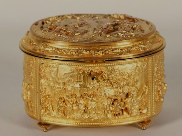 Antica scatola francese ovale in bronzo dorato, interamente cesellata e sbalzata a motivi di paesaggi e feste campestri, sorretta da quattro piedini