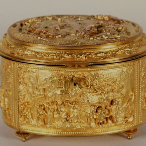 Antica scatola francese ovale in bronzo dorato, interamente cesellata e sbalzata a motivi di paesaggi e feste campestri, sorretta da quattro piedini