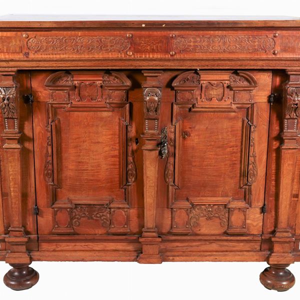 Antica credenza in legno chiaro con frontale intagliato, due sportelli e quattro gambe a cipolla