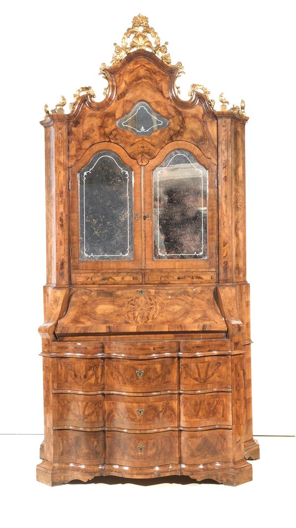 Venetian trumeau of the Louis XV line in walnut and walnut root, with inlaid threads and rosettes. The upper part with two engraved glass doors, compartments and drawers inside and a molded cymatium with golden friezes. The lower part with a flap forming a desk and three drawers underneath