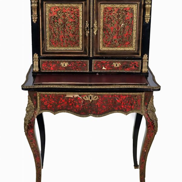 Bonheur du jour francese Napoleone III (1852-1870), in legno ebanizzato con intarsi alla maniera Boulle e fregi e guarnizioni in bronzo dorato e cesellato. La parte superiore a due sportelli, la parte inferiore con pianetto scorrevole formante scrittoio e tiretto sottostante, quattro gambe ricurve. Difetti