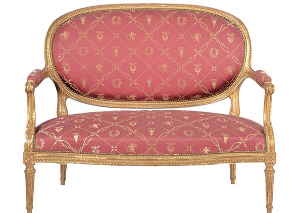 Antique small French sofa of the Louis XVI line, in gilded wood and carved with neoclassical motifs, cover in purple red fabric with designs of cupids, amphorae and laurel wreaths. The fabric is worn