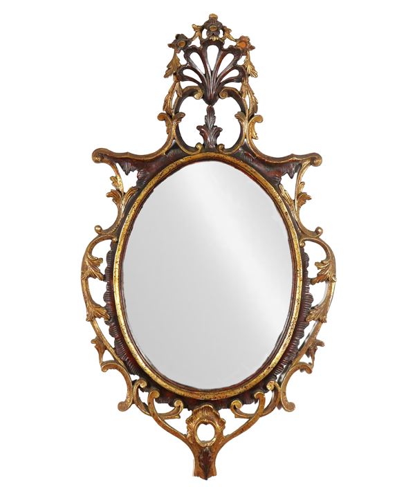 Oval mirror in patinated and mecca-gilded wood, with cymatium and friezes carved with scrolls of acanthus leaves