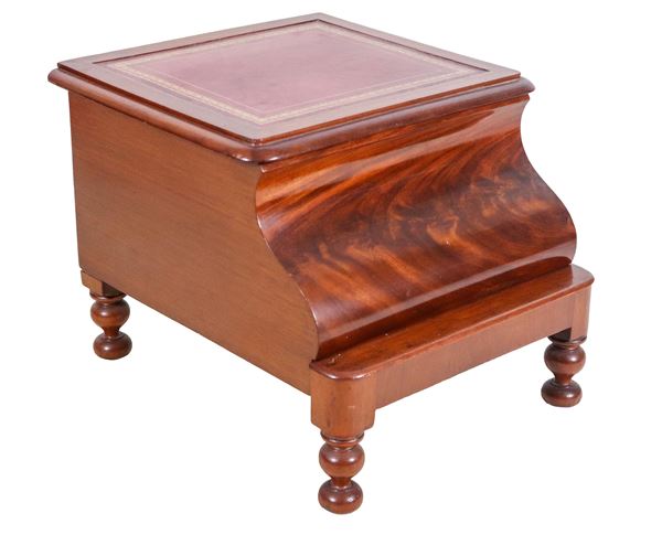 Antique English commode in mahogany from the Victorian era, with liftable top and white ceramic cup inside with lid, removable base with footrest. The upper surface and the base surface covered in red leather.