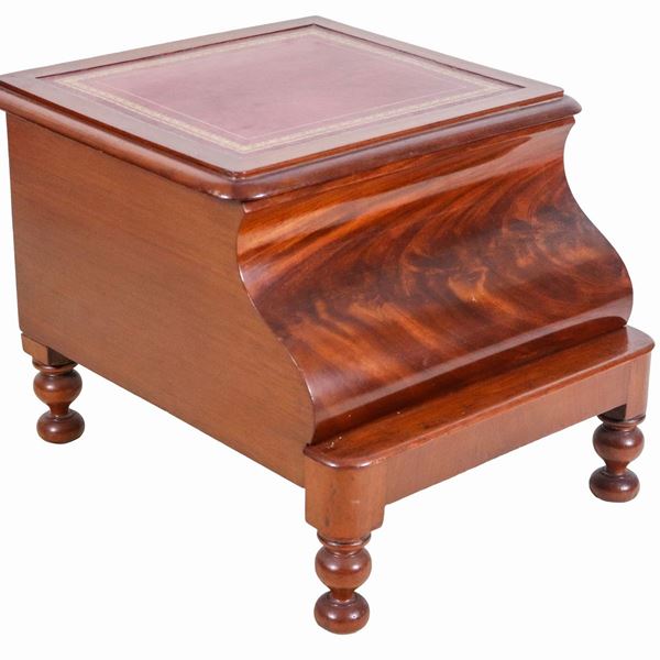 Antique English commode in mahogany from the Victorian era, with liftable top and white ceramic cup inside with lid, removable base with footrest. The upper surface and the base surface covered in red leather.