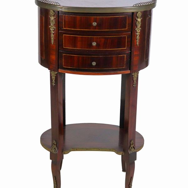 Gueridon francese a forma ovale in mogano, con intarsi a marqueterie, tre tiretti e quattro gambe riunite da pianetto sottostante