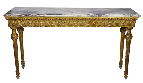 Consolle francese di linea Luigi XVI, in legno dorato e intagliato a motivi di fiocchi e rosoni, quattro gambe a cono scannellato e piano in marmo grigio venato