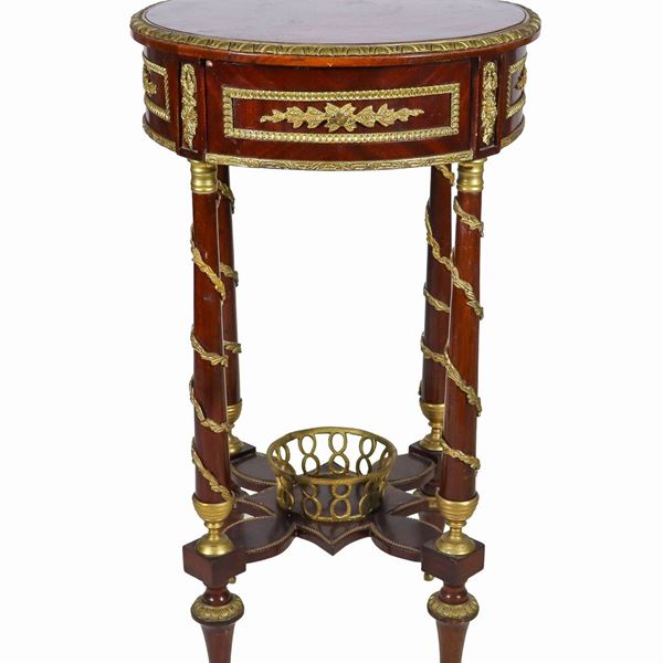Tavolo francese da centro a forma tonda di linea Impero, in ebano viola e mogano, con guarnizioni e fregi in bronzo dorato e cesellato a motivi neoclassici, un tiretto centrale e quattro gambe a colonna riunite da crociera sormontata da cesto in bronzo
