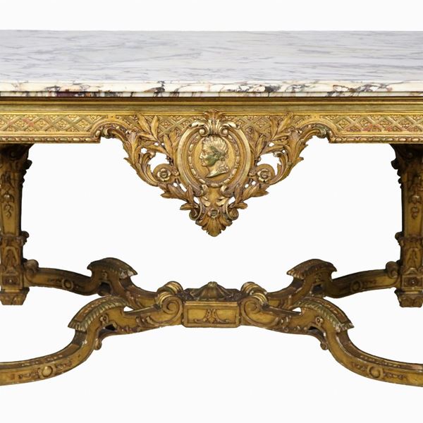 Tavolo da centro francese di linea Luigi XIV a forma rettangolare, in legno dorato e riccamente intagliato a motivi di ricci, foglie d'acanto, medaglioni e rosoni, quattro gambe riunite da crociera centinata e piano in marmo pavonazzetto. Il marmo presenta mancanza ad un angolo