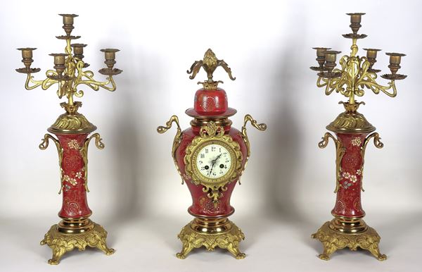 Trittico francese Liberty, pendola e due candelabri a cinque fiamme, in bronzo dorato, sbalzato e cesellato, rivestito con smalti a motivi di ghirlande floreali su fondo rosso bordeaux