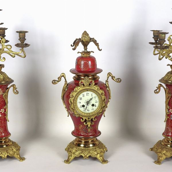 Trittico francese Liberty, pendola e due candelabri a cinque fiamme, in bronzo dorato, sbalzato e cesellato, rivestito con smalti a motivi di ghirlande floreali su fondo rosso bordeaux