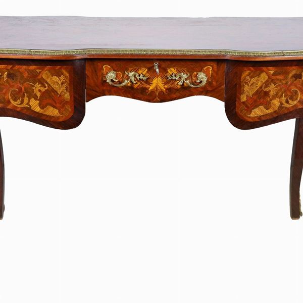 Scrivania francese da centro di linea Luigi XV, in ebano viola e bois de rose, interamente intarsiata con vari legni pregiati a motivi di volute di intrecci floreali, guarnizioni, fregi e sculture muliebri in bronzo dorato, sbalzato e cesellato, un tiretto centrale e quattro gambe ricurve