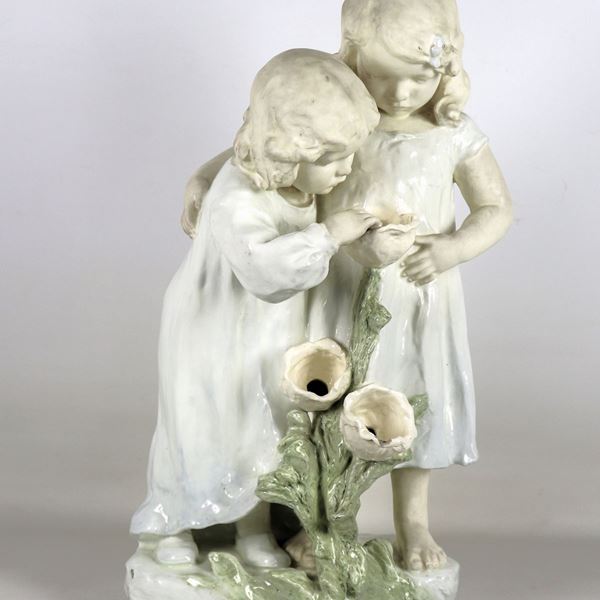 "Bambine con fiori", gruppo in ceramica e porcellana morbida smaltata, firmato Augmuller Ludwig (1876-?), modellista e scultore del Periodo Art Nouveau. Lieve mancanza