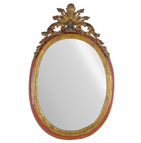 Antica specchiera ovale in legno laccato e dorato a mecca, con cimasa intagliata a motivi floreali e ricci, specchio al mercurio. Lievi difetti