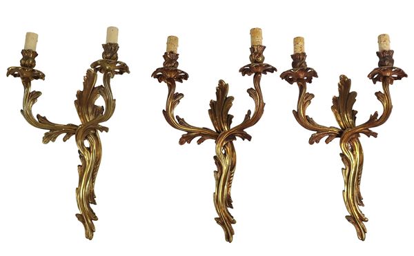 Lotto di tre appliques francesi di linea Luigi XV in bronzo dorato e sbalzato, due luci ciascuna