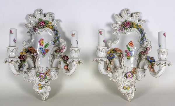 Coppia di appliques in porcellana Capodimonte, con decorazioni policrome a rilievo di ghirlande floreali, due luci ciascuna. Lievi difetti