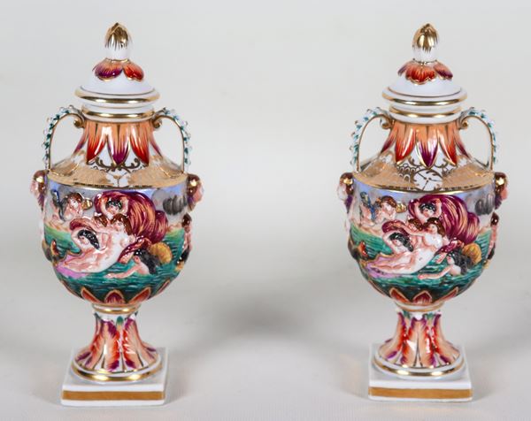 Coppia di piccole anfore in porcellana policroma e dipinta di Capodimonte, con scene mitologiche a rilievo